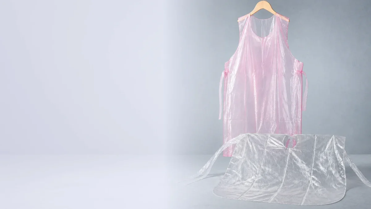Disposable pink PE apron and clear salon cape on a light cool gray-blue studio background