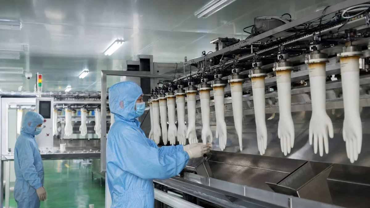 Workers operating automated disposable glove production machinery inside a clean modern factory cleanroom